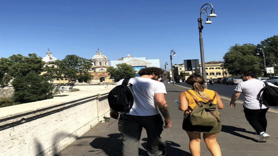 A group of people, embarked on a real travel adventure in the enchanting city of Rome, are happily walking on a bridge.
