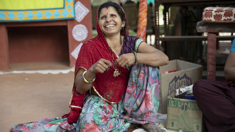 A woman in a red sari celebrating International Women's Day, sitting on the ground.