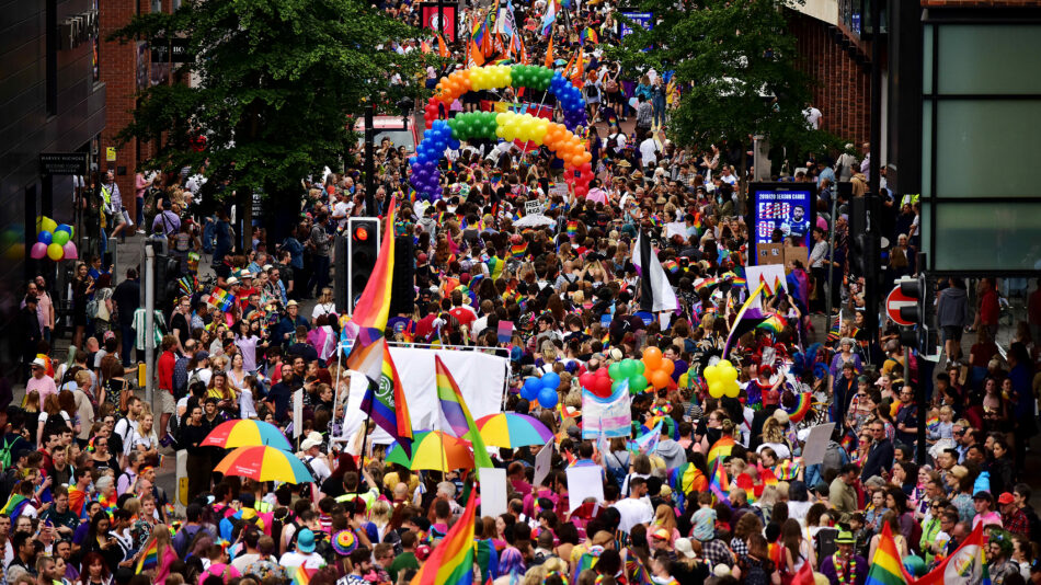 A crowd of people participating in a pride event, proudly walking down a street with rainbow flags.