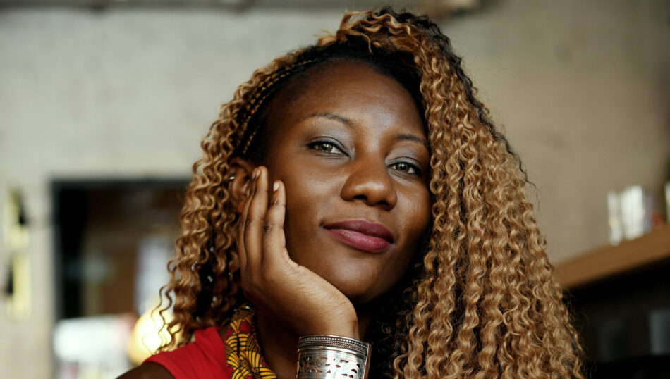 A young African woman with curly hair posing for a photo during her LGBTQIA+ travel adventure.