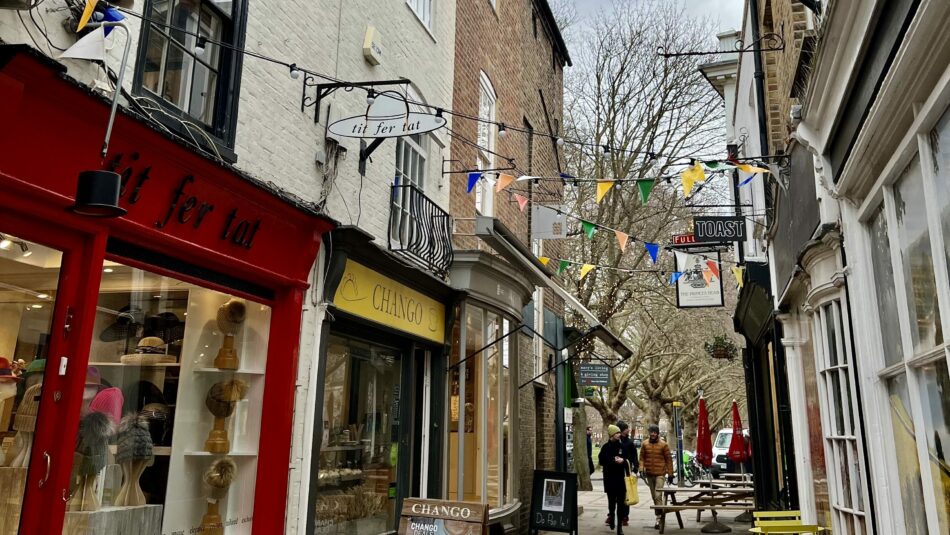 A narrow street with shops and a person walking down it - potentially a Ted Lasso filming location.