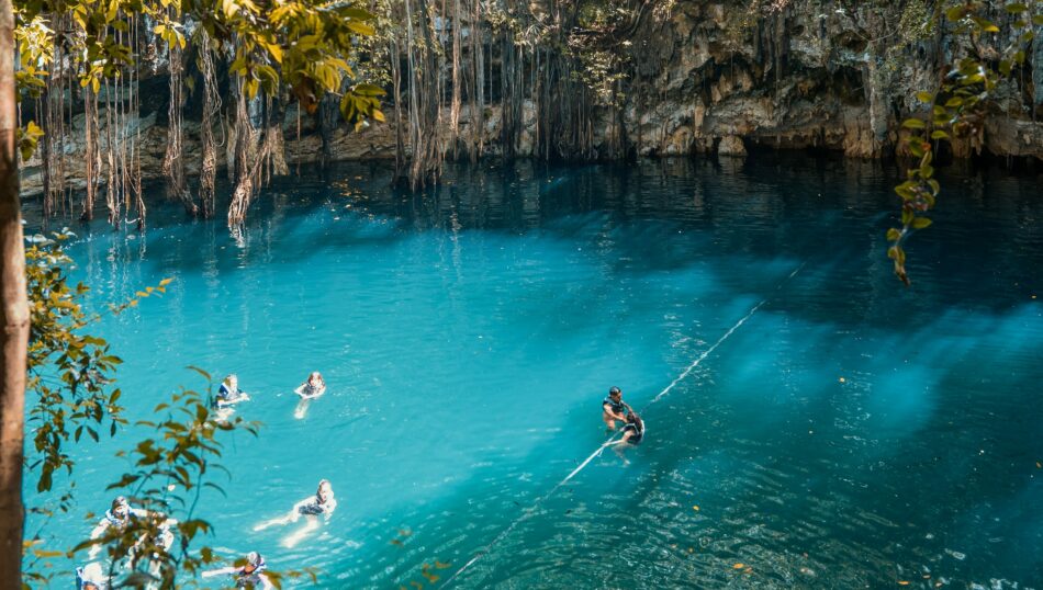 A group of people are going on an adventure swimming in the blue water of a cave during their vacations.