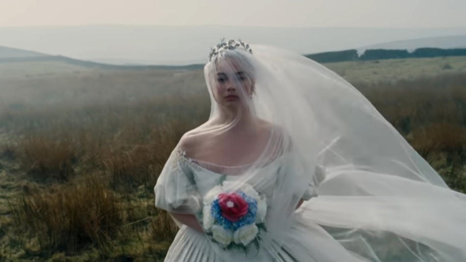 Margot Robbie in field carrying bouquet and dressed in white wedding gown in Wuthering Heights