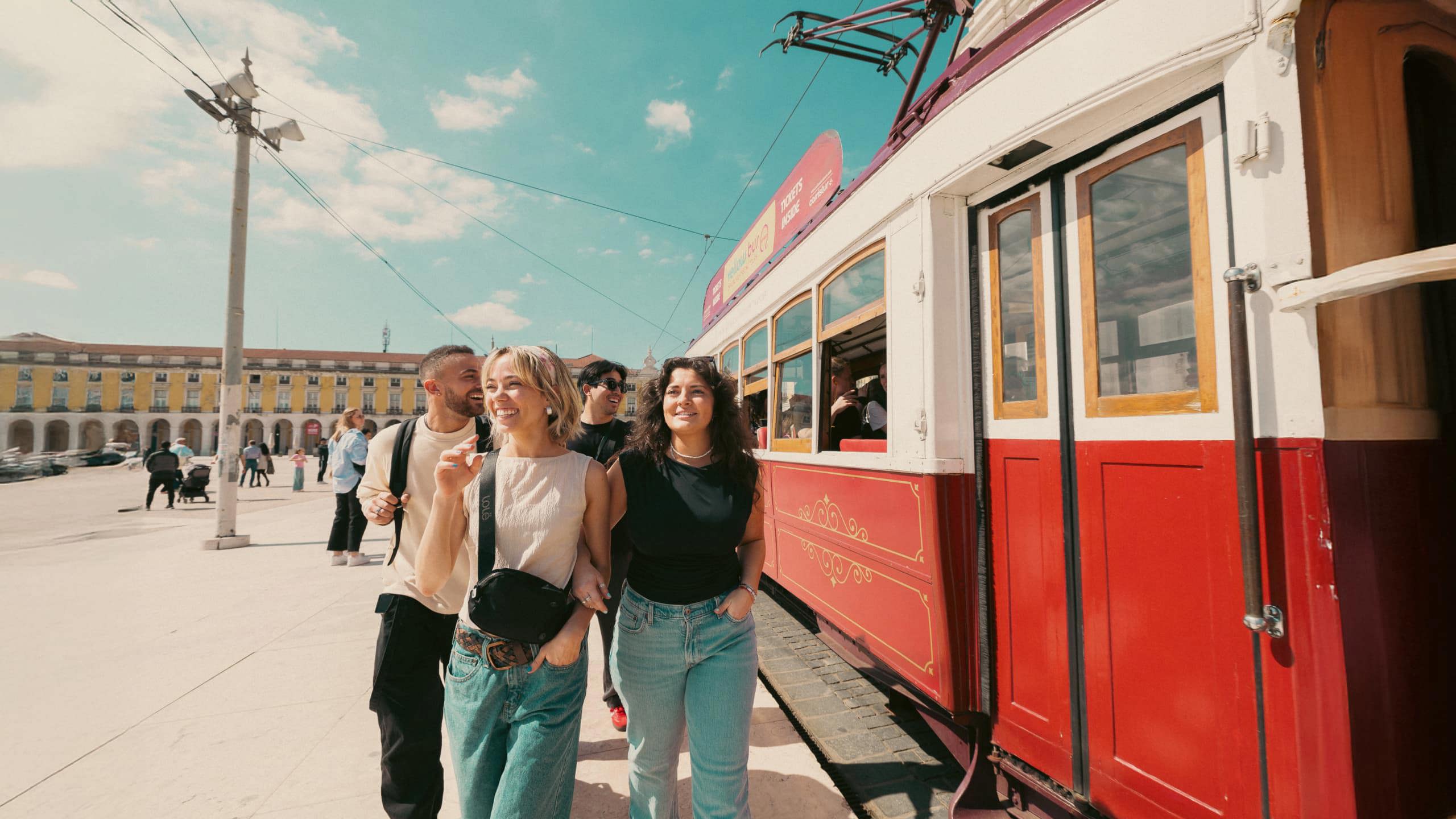 Young travellers next to a vintage red tram at Praça do Comércio Lisbon Portugal - Contiki Spain and Portugal Tour